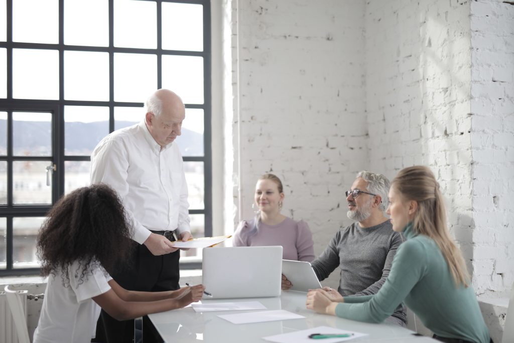 Concentrated man talking with colleague about business project and explaining details while standing near table and window in modern office
